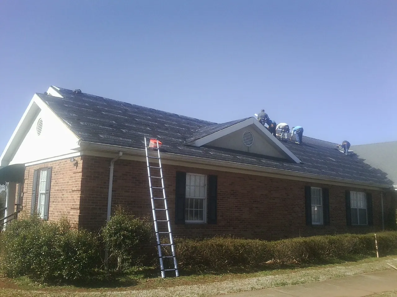 Crew tearing shingles off a brick ranch roof with a ladder set — Metal Roof Repair work by our crew in Medfield