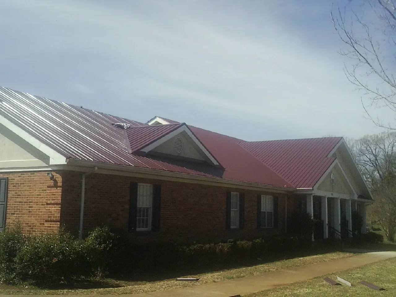 Red metal roof with gabled entries on a long brick building, from a Hail Damage Roof Repair job in Medfield