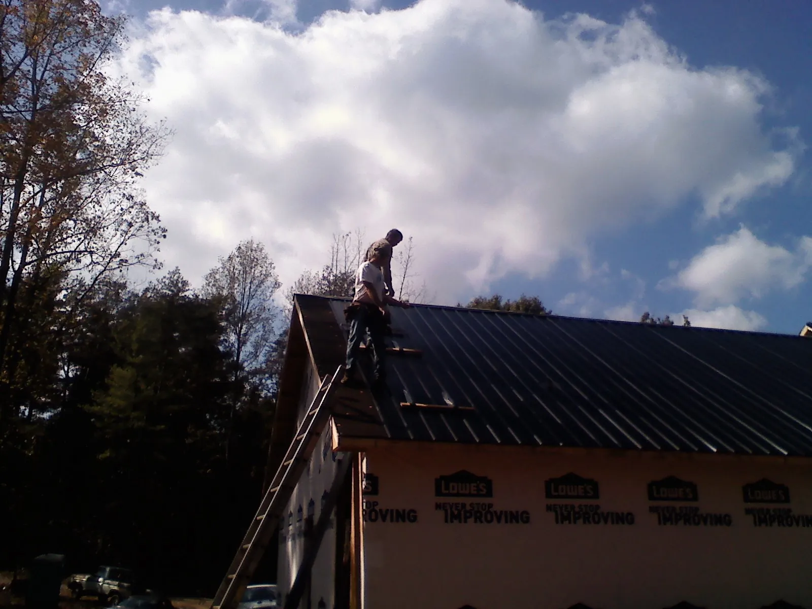 Roofer fastening dark metal panels high against a cloudy sky, from a Roof Inspection job in Medfield