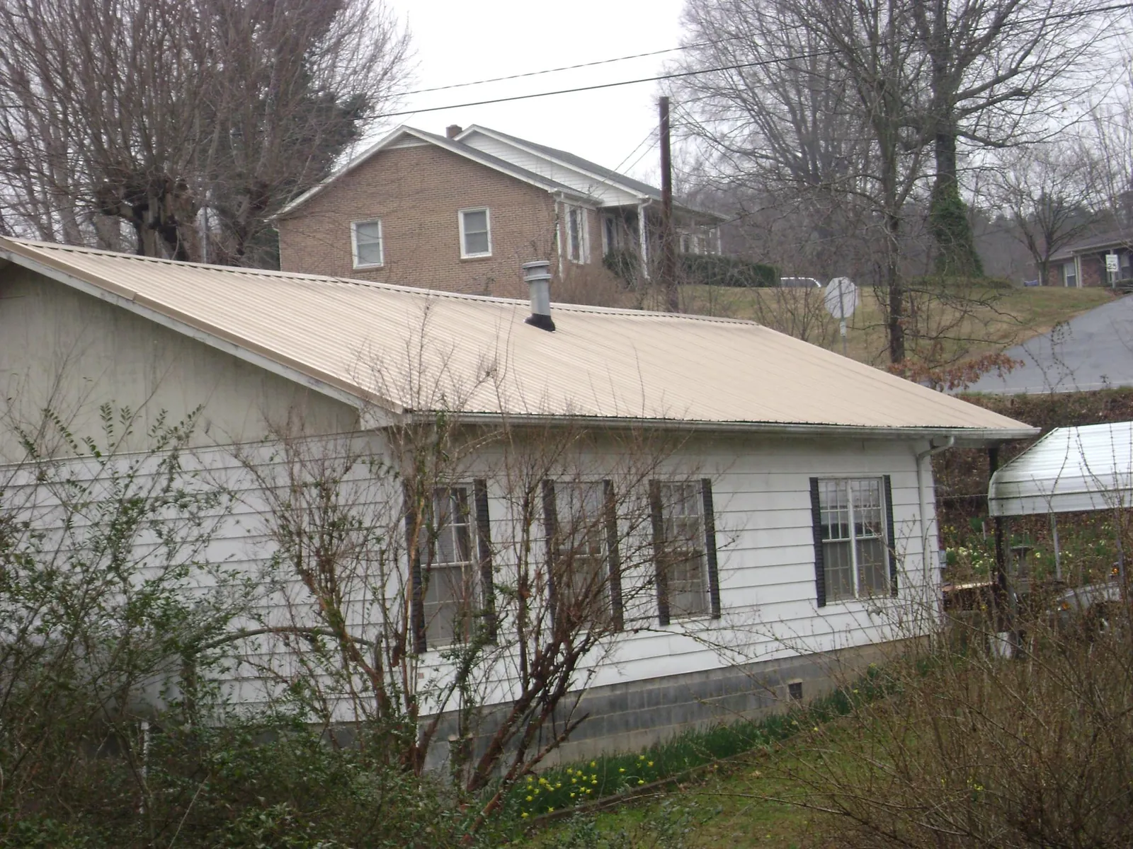Tan metal roof on a white sided house set into a hillside — Commercial Roofing by Roofing Brothers in Medfield
