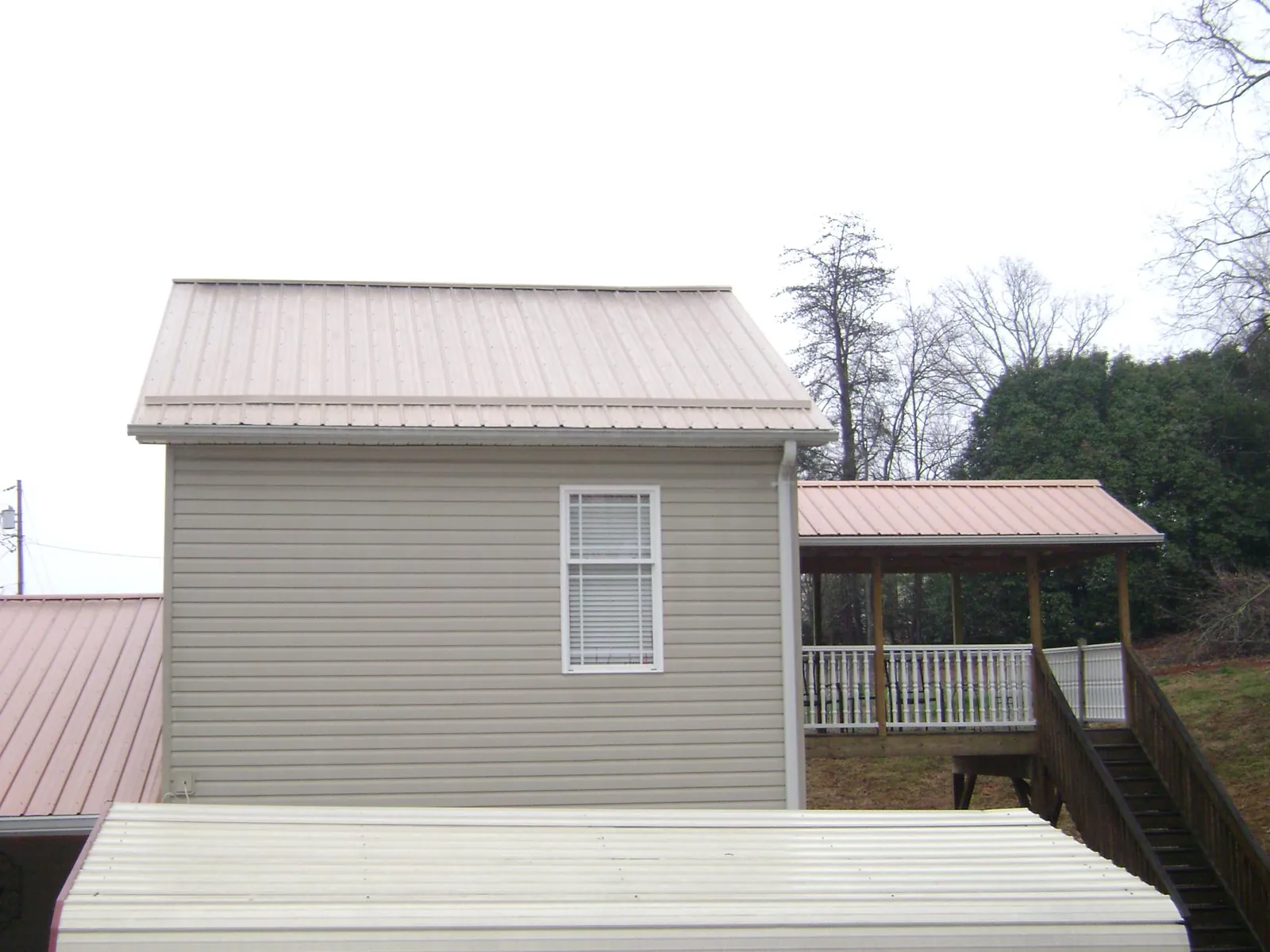 Tan metal roofs on a two story addition and attached porch, from a Roof Replacement job in Medfield